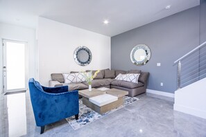 A modern living room with a sectional sofa, a blue armchair, and two wall mirrors.