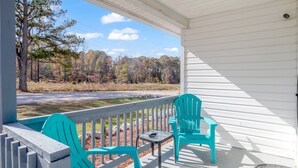 A porch with turquoise chairs and a table, overlooking a road and trees. - Beachy Getaway • Clean, Private 3BR (Wendell)