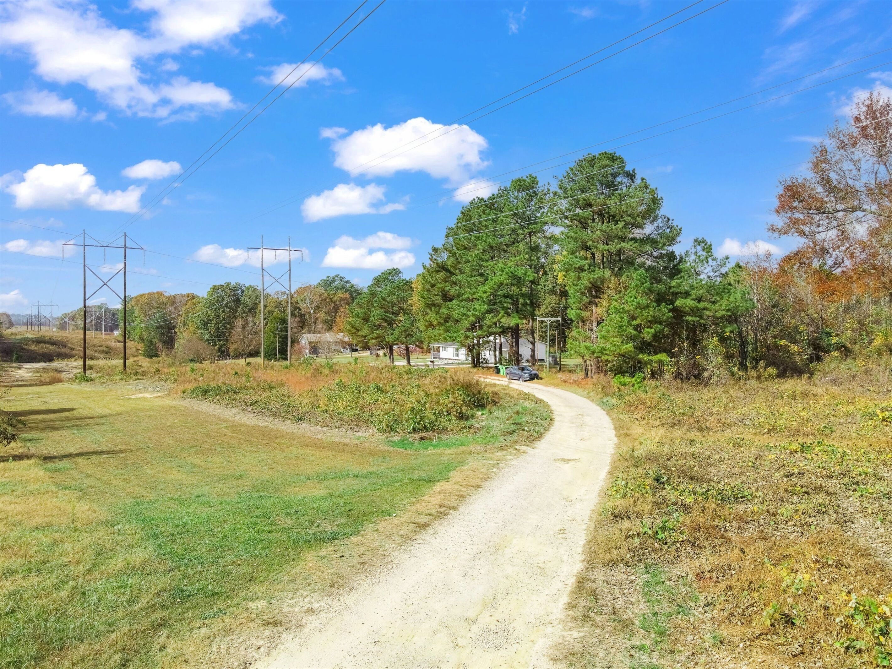 A rural road curving through a landscape with a house and trees.