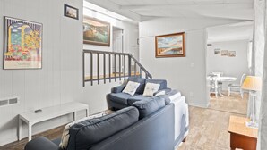 Un salon moderne avec un canapé gris, un banc blanc et un escalier menant à une autre pièce.