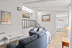 Una sala moderna con un sofá gris, un banco blanco y una escalera que lleva a otra habitación.