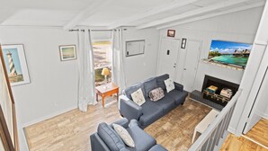 A living room with a grey sofa, a fireplace, and a TV displaying a tropical scene. - Beachy Getaway • Clean, Private 3BR (Wendell)