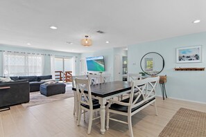A living room with a dark wooden dining table, white chairs, a large flat-screen TV, and a light blue wall. - ⭐Fabulous Backyard~Walk to Crystal Beach~3BR Eternal Summer (Destin)