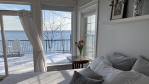 A bedroom with a large bed, a view of a snowy deck, and a window with a view of the water. - Smith's Lake House 4 bedroom, enjoy spectacular sunrises, 2 bathroom, built 2021 (Penn Yan)