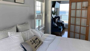A bedroom with a large bed, a view of the ocean through a door, and a chair by the window. - Smith's Lake House 4 bedroom, enjoy spectacular sunrises, 2 bathroom, built 2021 (Penn Yan)