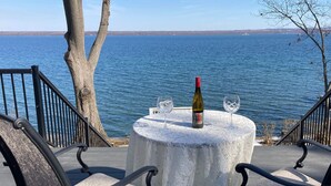 A table with a bottle and two glasses on a deck overlooking a body of water. - Smith's Lake House 4 bedroom, enjoy spectacular sunrises, 2 bathroom, built 2021 (Penn Yan)