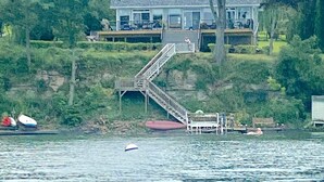 A lakeside house with a dock, a staircase leading to the main building, and a boat in the water. - Smith's Lake House 4 bedroom, enjoy spectacular sunrises, 2 bathroom, built 2021 (Penn Yan)