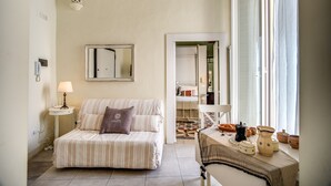 Una camera accogliente con un letto a righe, un comodino con una lampada, uno specchio appeso al muro e una finestra con tende.