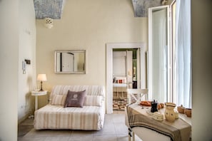 Une chambre confortable avec un lit à rayures, une table de chevet avec une lampe, un miroir au mur et une fenêtre avec des rideaux.