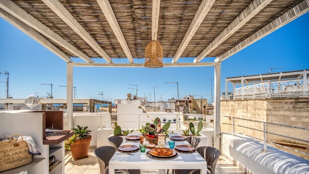 Una terrazza sul tetto con un tavolo apparecchiato per mangiare, circondata da piante in vaso e una lampada a sospensione.
