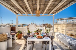 Eine Dachterrasse mit Esstisch, umgeben von Topfpflanzen und einem hängenden Licht.