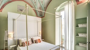 Un letto a baldacchino con tenda bianca, un piccolo comodino e una lampada fissata al muro.
