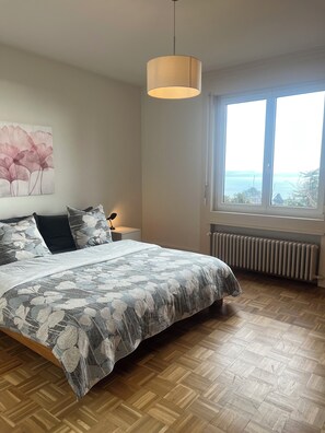 Une chambre à coucher comprenant un lit, une table de chevet, une lampe, un radiateur et une fenêtre donnant sur un beau paysage.