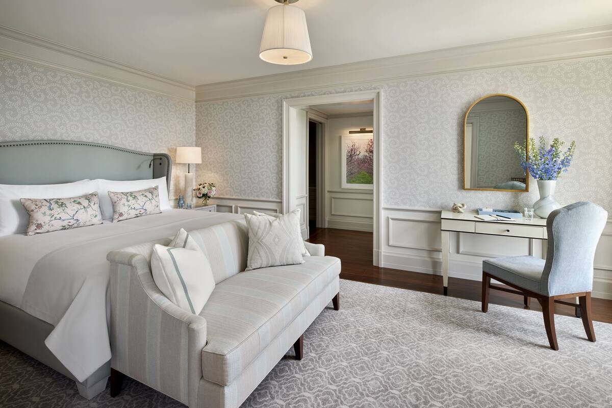 Une chambre d’hôtel avec un grand lit, un coin salon avec un canapé, un bureau avec une chaise et un miroir au mur.