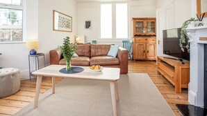 A living room with a brown leather sofa, a white coffee table, a blue chair, a wooden cabinet, and a television.