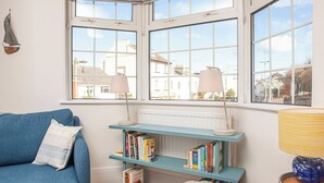 A cozy room with a blue sofa, a bookshelf, and a bay window with two lamps.