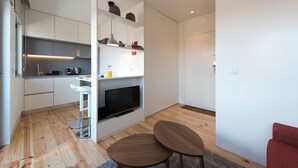 A modern kitchen with white cabinets, a built-in oven, and a flat-screen TV. There are two stools and a small table in the living area. - Gorgeous Modern Flat w/ Balcony by LovelyStay (Porto)