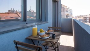 A balcony with a table set for breakfast, including croissants, a glass of juice, and a bowl of fruit. - Gorgeous Modern Flat w/ Balcony by LovelyStay (Porto)