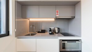 Uma cozinha compacta com micro-ondas embutido, cafeteira e chaleira no balcão.
