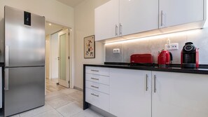 Une cuisine moderne dotée d’un réfrigérateur en acier inoxydable, de meubles blancs, d’un plan de travail noir et d’appareils électroménagers rouges.