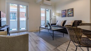 Ein modernes Wohnzimmer mit einer Couch, einem Couchtisch und Korbstühlen. Ein großes Schiebeglasfenster führt in einen Außenbereich.