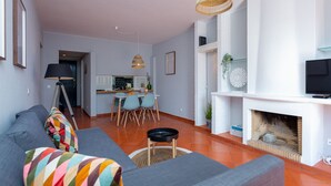 A modern living room with a gray sofa, a dining area with a table and chairs, a fireplace, and a television. - Gorgeous 2BDR W/Patio & Pool by LovelyStay (Vilamoura)