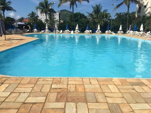 Une piscine dont le fond est recouvert de carrelage, entourée de chaises longues et de parasols, avec des palmiers en arrière-plan.