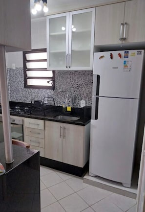A kitchen with a gas stove, sink, and white refrigerator. - cond. Wembley Tennis Ubatuba apartment with a view of the pool, 150 meters from the beach. Dolphins (Ubatuba)