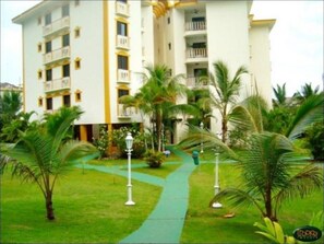 Ein Hotel mit mehreren Etagen, Balkonen und einem gepflegten Garten mit Palmen und einem Weg.