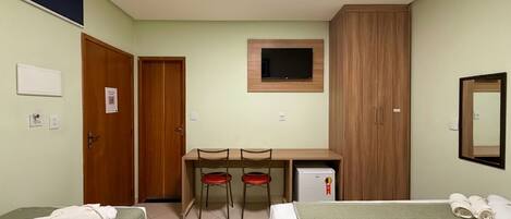 A hotel room with two beds, a desk with chairs, a TV, a mirror, and a small refrigerator.
