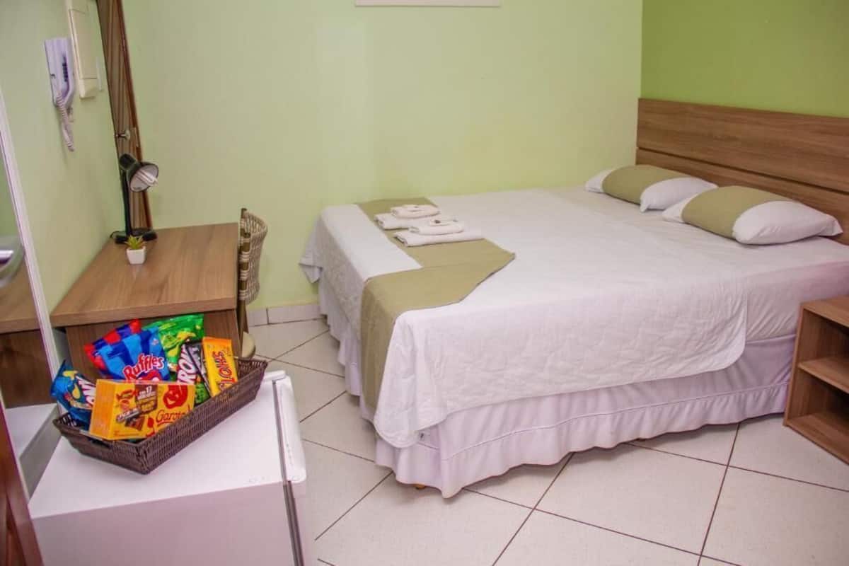 Een hotelkamer met een bed, een nachtkastje met lamp, een mand met snacks en een houten hoofdbord.