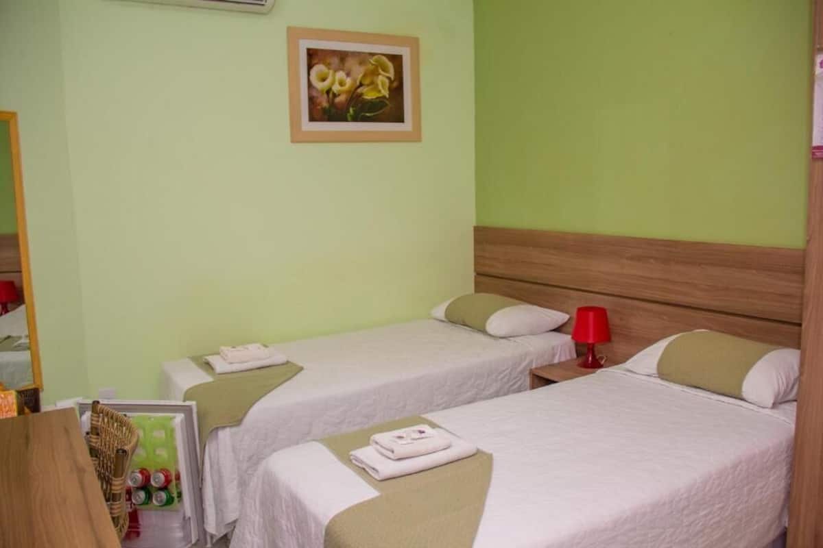 Een hotelkamer met twee eenpersoonsbedden, een houten hoofdbord, een rode lamp en een lijst met een afbeelding aan de muur.