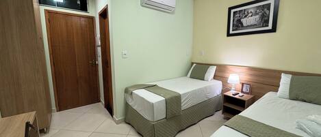 Quarto de hotel com duas camas, um guarda-roupa de madeira, um aparelho de ar condicionado e um quadro emoldurado na parede.