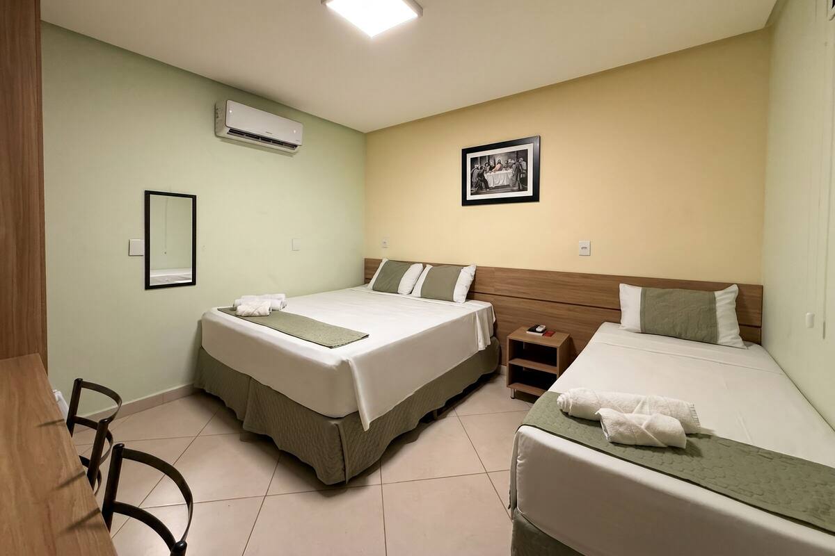 Een hotelkamer met twee bedden, een houten hoofdeinde, een klein nachtkastje, een airconditioner, een lijst met een afbeelding aan de muur en een fiets in de hoek.