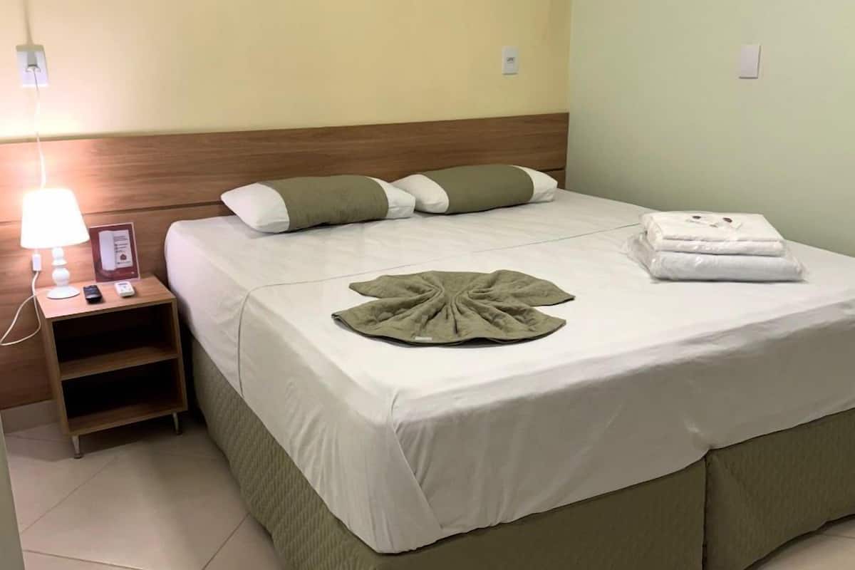 Een hotelkamer met een bed, een nachtkastje met een lamp en een opgevouwen handdoek op het bed.