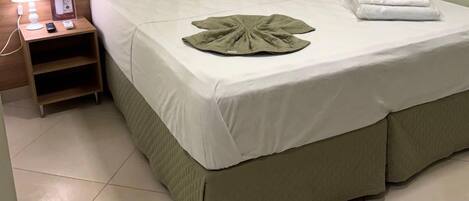 Une chambre d’hôtel avec un lit, une table de chevet avec une lampe et une serviette pliée posée sur le lit.