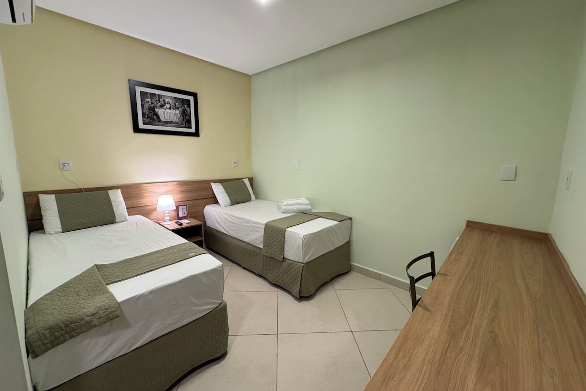 Een hotelkamer met twee bedden, een houten tafel en een lijst met een foto aan de muur.