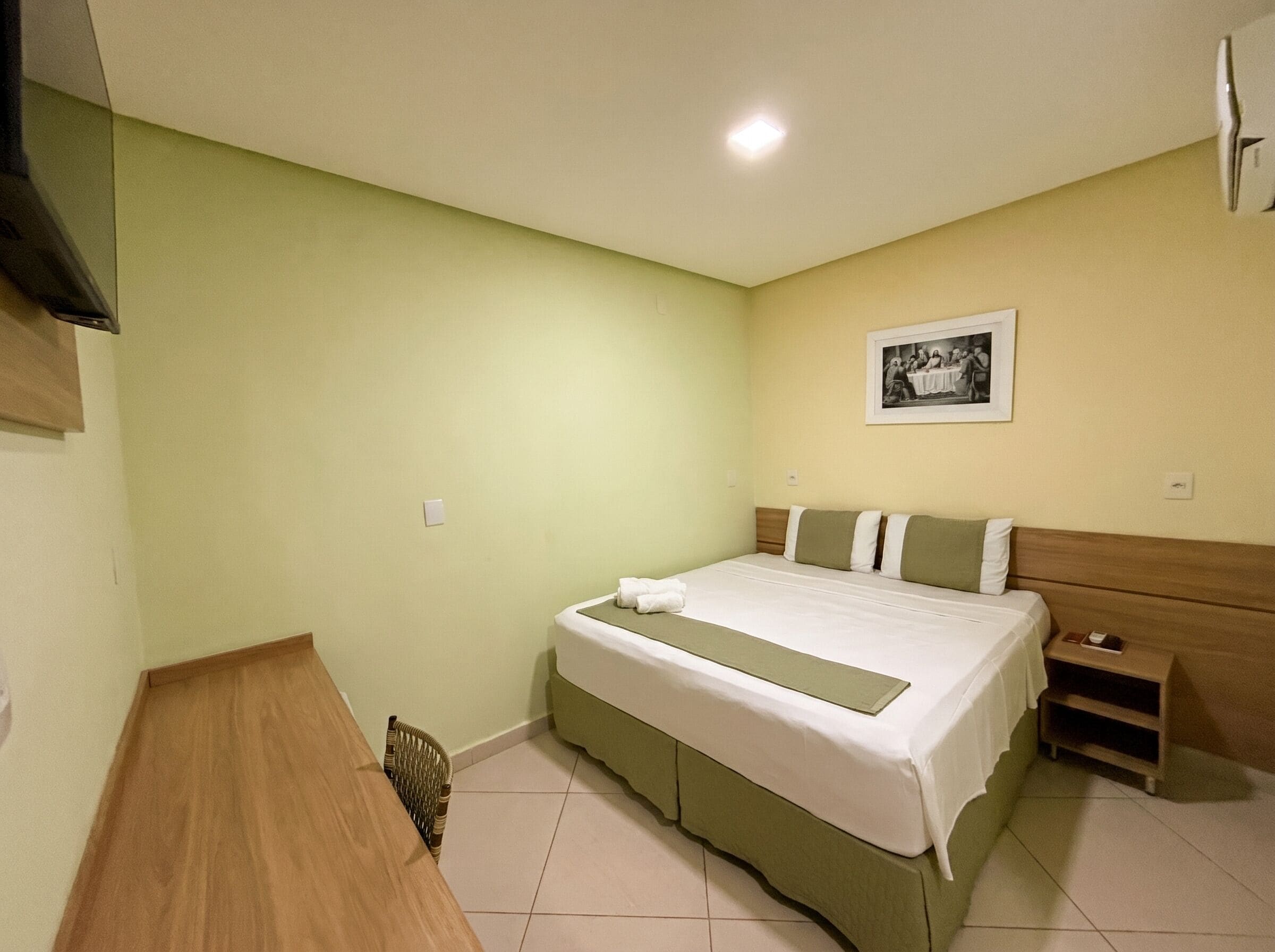 Una habitación de hotel con cama, mesita de noche, silla e imagen enmarcada en la pared.