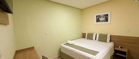 Una habitación de hotel con cama, mesita de noche, silla e imagen enmarcada en la pared.
