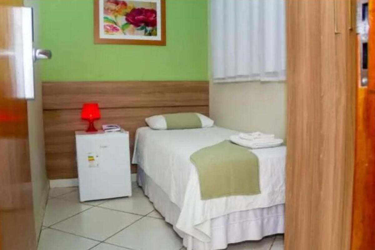 Een kamer met een bed, een nachtkastje, een rode lamp en een klein wit apparaat.
