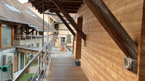 A wooden balcony with a metal railing, wooden beams, and a view of neighboring buildings. - Le Domaine du Verger, Chambres D'hôtes (Osenbach)
