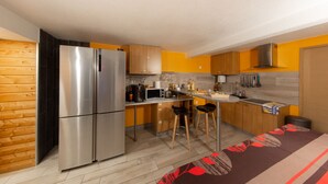 A compact kitchen with a stainless steel refrigerator, wooden cabinets, and a bar stool. - Le Domaine du Verger, Chambres D'hôtes (Osenbach)