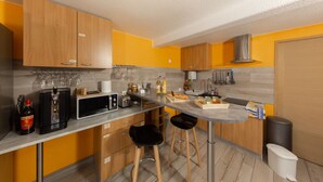 A modern kitchen with wooden cabinets, a microwave, a coffee machine, and two bar stools. - Le Domaine du Verger, Chambres D'hôtes (Osenbach)