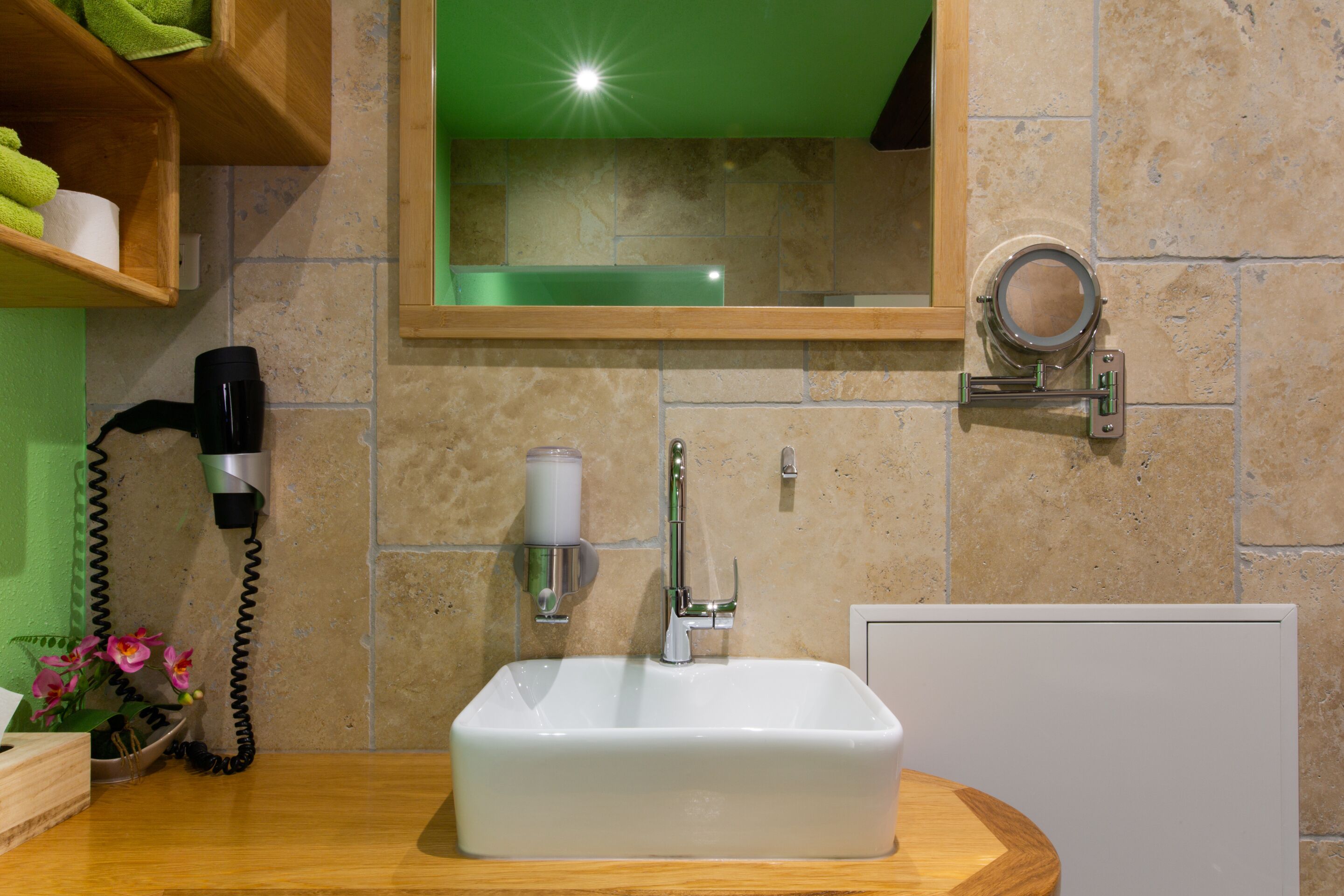 Un baño con un lavabo blanco, un espejo, un dispensador de toallas y un secador de pelo sobre una encimera de madera.