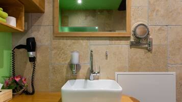 Un baño con un lavabo blanco, un espejo, un dispensador de toallas y un secador de pelo sobre una encimera de madera.