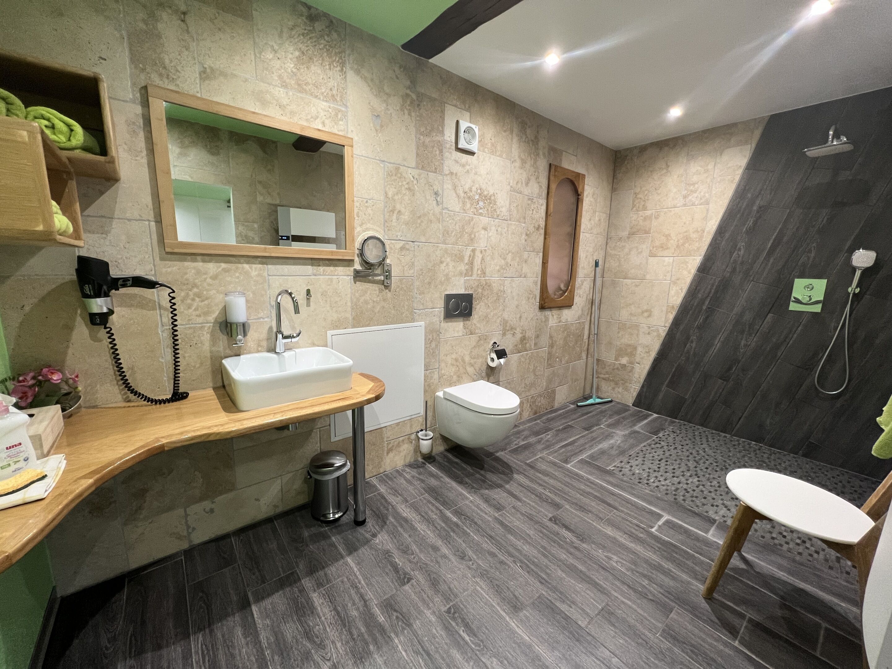 A modern bathroom with a wooden vanity, a white sink, a toilet, and a shower area.