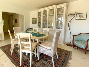 A dining area with a round table, white chairs, a patterned rug, and a cabinet with glass doors.