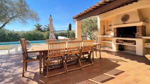 An outdoor patio with a wooden table and chairs, a barbecue grill, and a pool in the background. - Villa 10 people-Private Pool-250m from the sea (Fréjus)