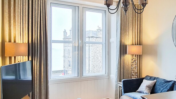 A room with a large window, a flat-screen TV, a sofa, a table, and two lamps.