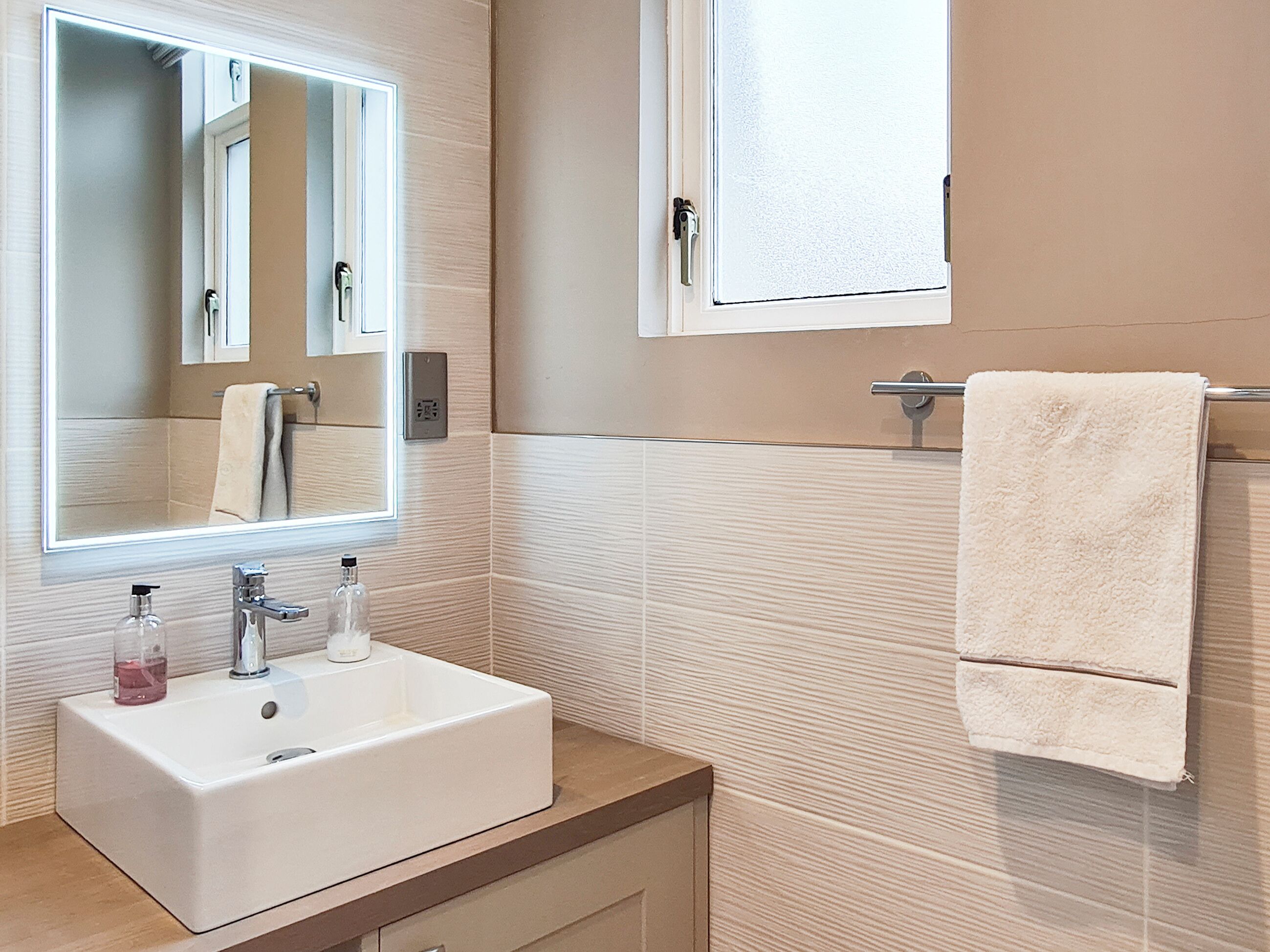 Une salle de bain avec un lavabo blanc, un miroir, un porte-serviettes et une fenêtre.